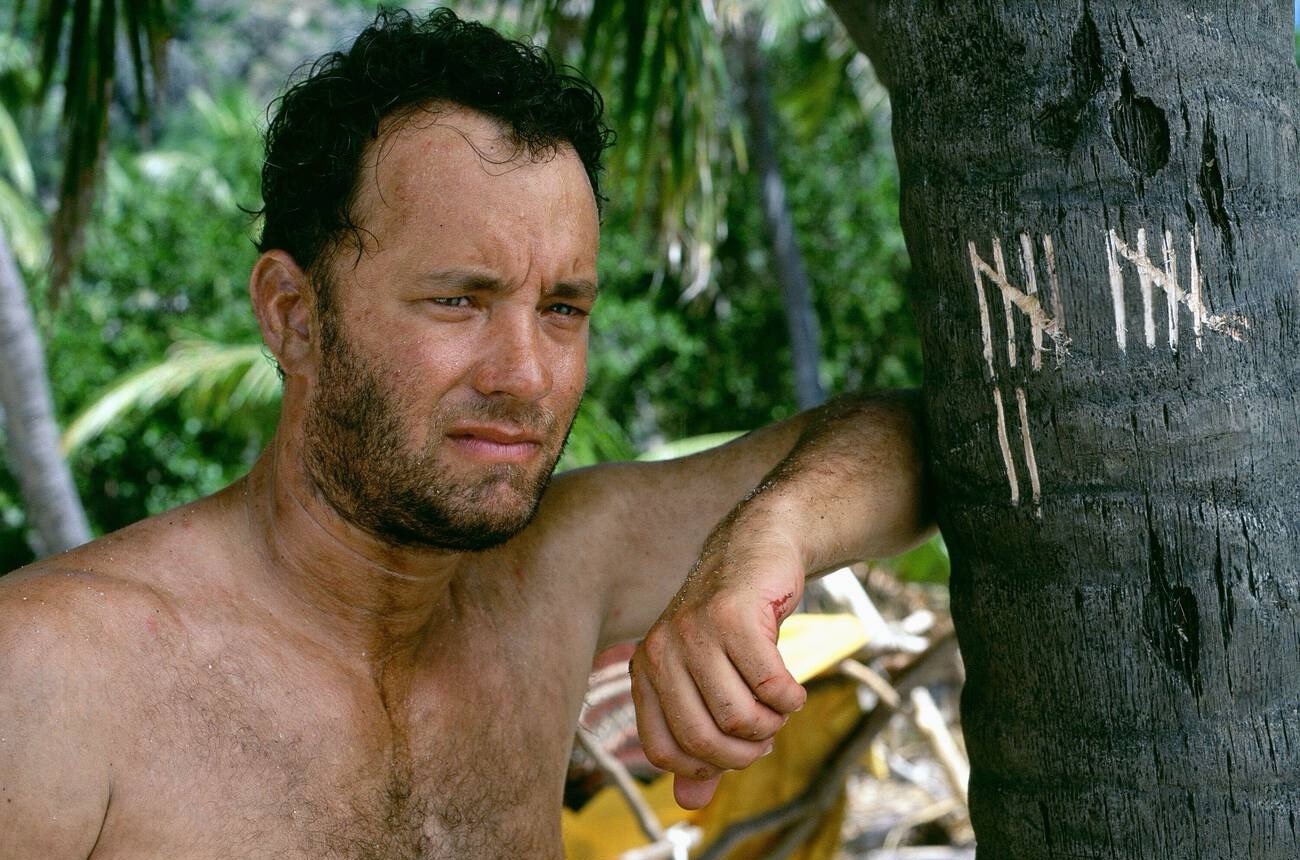 Chuck lost in thought, leaning against a palm tree.